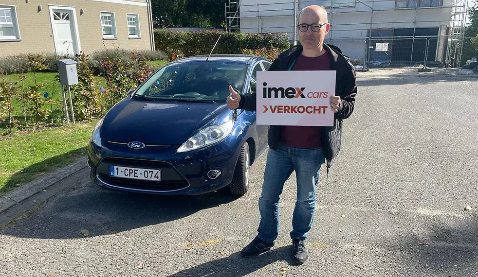 Verkoper met Imex Cars ‘VERKOCHT’ bord naast verkochte Ford – verkoop je auto in België